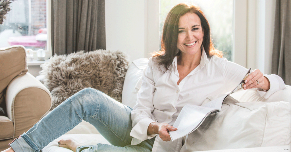 Smiling woman sits on a couch while holding a magazine.