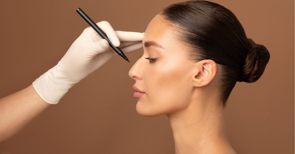 A woman undergoing pre-surgical markings by a doctor in preparation for rhinoplasty. (model)
