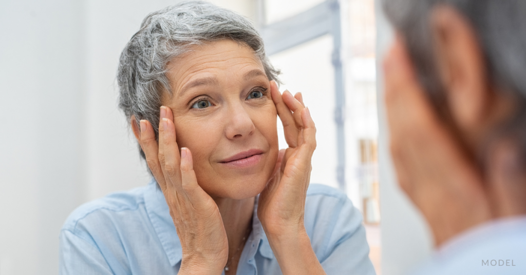 A mature woman looking in the mirror and touching her skin (model)