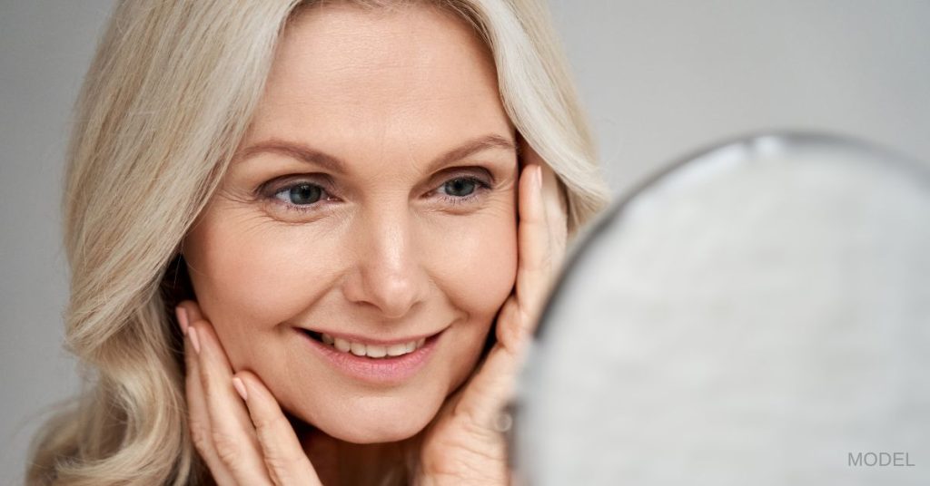 Beautiful middle-aged woman smiles while looking in the mirror. (Model)