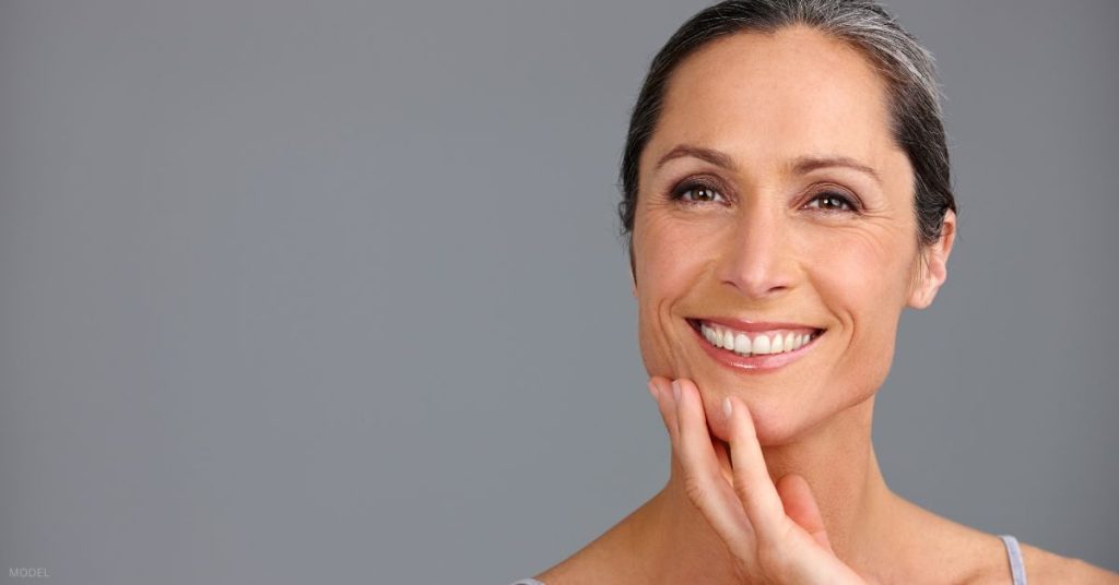 Woman smiling with her hand on her chin. (Model)
